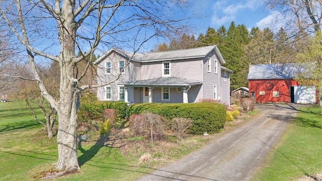 traditional home with an outdoor structure, driveway, a porch, and a front lawn