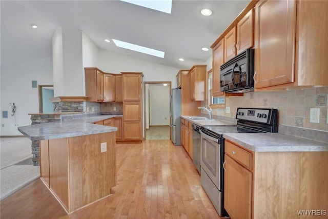 kitchen with stainless steel appliances, a peninsula, a sink, lofted ceiling with skylight, and tasteful backsplash