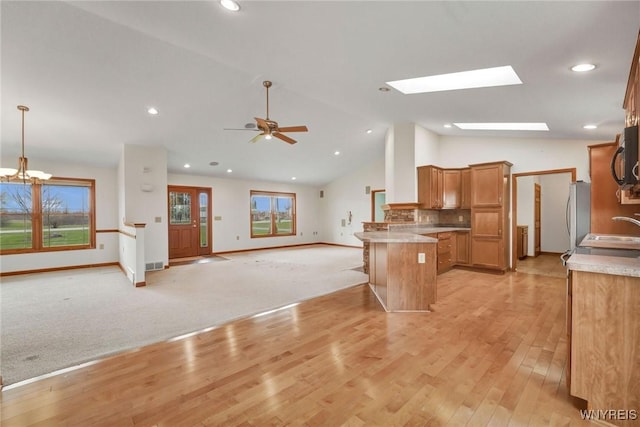 kitchen with brown cabinets, freestanding refrigerator, a peninsula, vaulted ceiling with skylight, and open floor plan