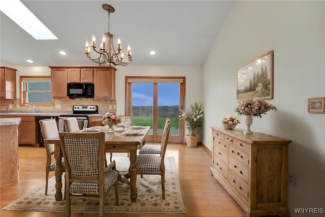 dining space with vaulted ceiling with skylight, a healthy amount of sunlight, light wood finished floors, and a notable chandelier