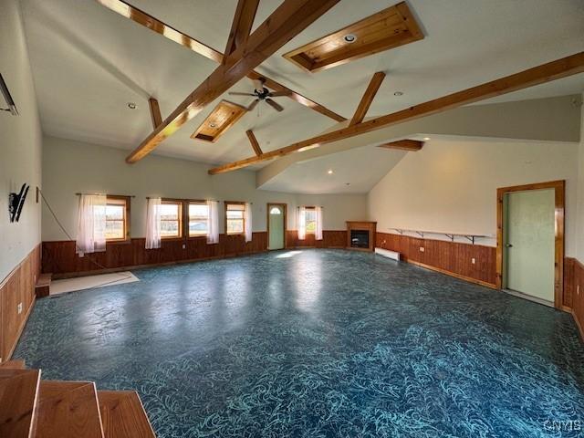 unfurnished living room featuring wood walls, a ceiling fan, lofted ceiling with beams, and wainscoting