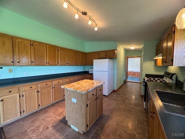 kitchen featuring a center island, a sink, white appliances, stone finish flooring, and under cabinet range hood
