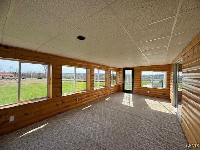unfurnished sunroom with wood walls, a drop ceiling, and carpet