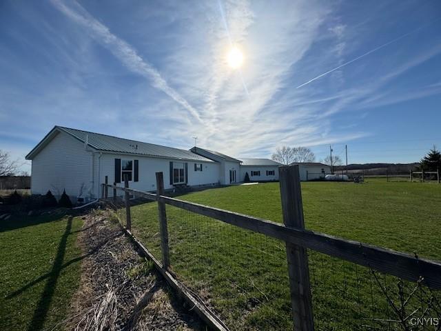 rear view of property with fence, a yard, and metal roof