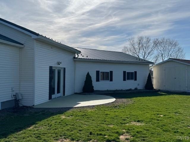 back of property with an outbuilding, metal roof, a yard, a shed, and a patio