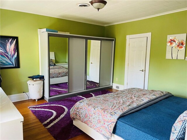 bedroom with wood finished floors, a closet, baseboards, ornamental molding, and visible vents