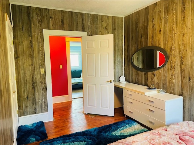 bedroom with wooden walls, wood finished floors, crown molding, and baseboards