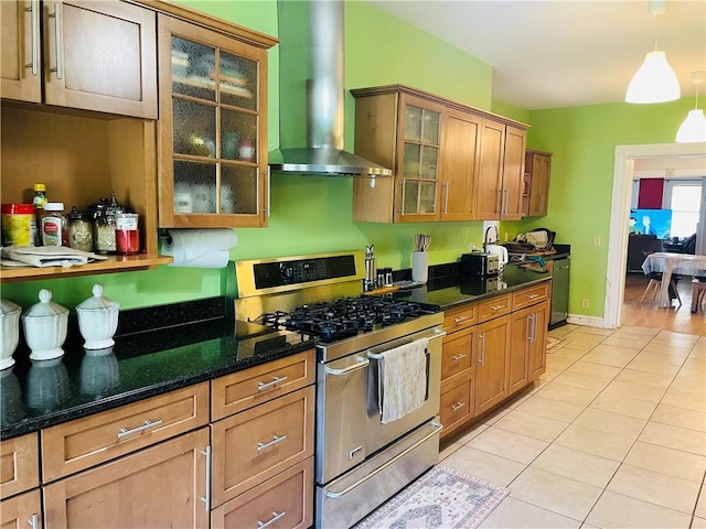 kitchen with wall chimney range hood, dark stone countertops, light tile patterned floors, dishwasher, and gas stove