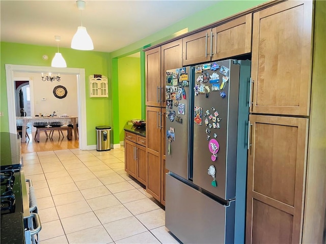 kitchen featuring dark countertops, light tile patterned flooring, freestanding refrigerator, gas stove, and pendant lighting