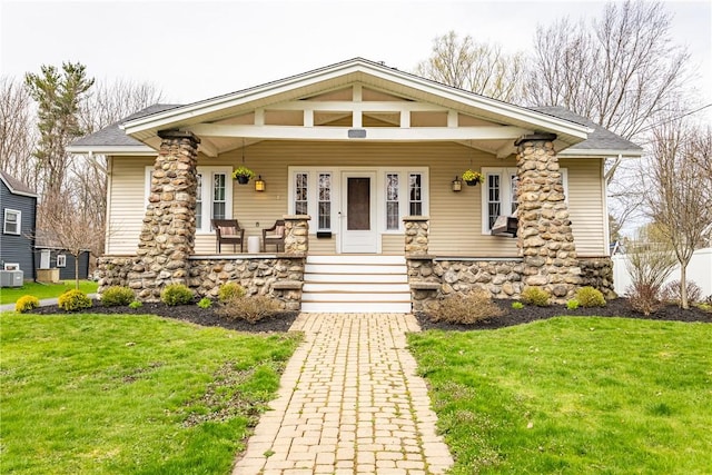 view of front of house with a front lawn, roof with shingles, a porch, and stone siding