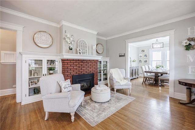 sitting room featuring baseboards, a brick fireplace, wood finished floors, and ornamental molding