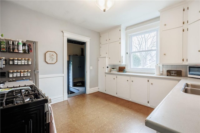 kitchen with light floors, light countertops, baseboards, gas range, and white cabinetry