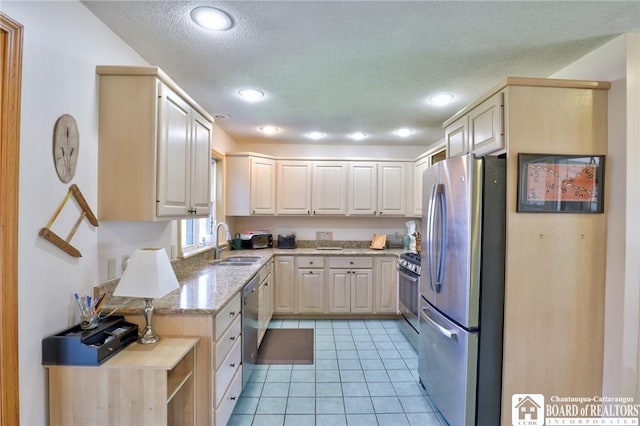 kitchen featuring light brown cabinetry, light stone counters, a sink, light tile patterned flooring, and appliances with stainless steel finishes