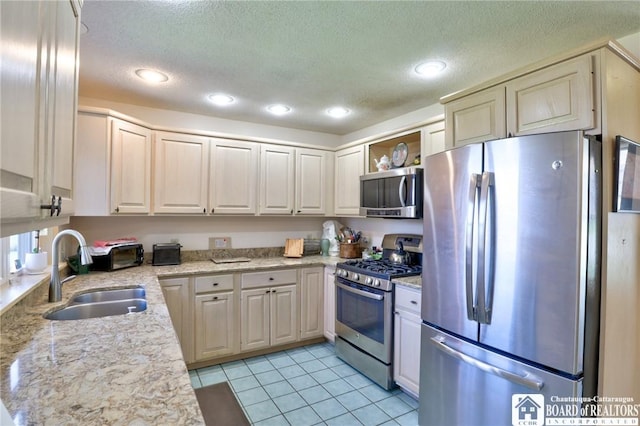 kitchen with open shelves, a sink, a textured ceiling, light tile patterned flooring, and appliances with stainless steel finishes