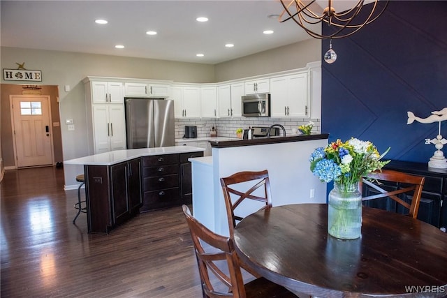 kitchen with dark wood finished floors, white cabinets, a kitchen breakfast bar, and stainless steel appliances