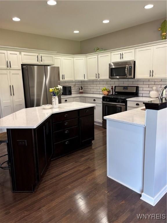 kitchen featuring a center island, appliances with stainless steel finishes, white cabinets, backsplash, and dark wood-style flooring