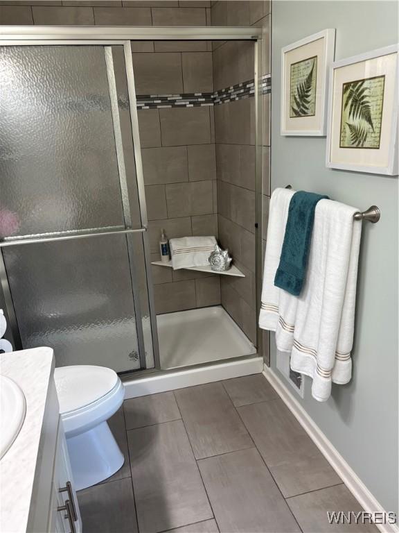 bathroom featuring baseboards, toilet, vanity, and a stall shower