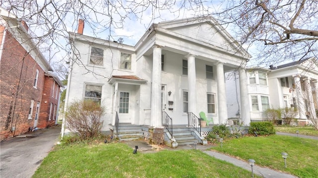 neoclassical home with a chimney, a front lawn, and stucco siding