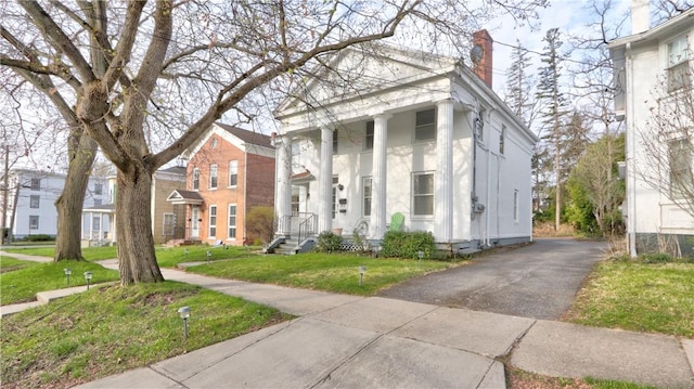 neoclassical home with a chimney, a front lawn, aphalt driveway, and stucco siding
