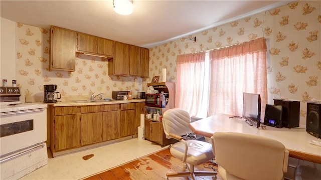 kitchen featuring wallpapered walls, light wood finished floors, white range with electric stovetop, light countertops, and a sink