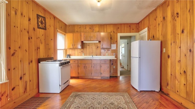kitchen with light countertops, wooden walls, a sink, white appliances, and light wood-type flooring