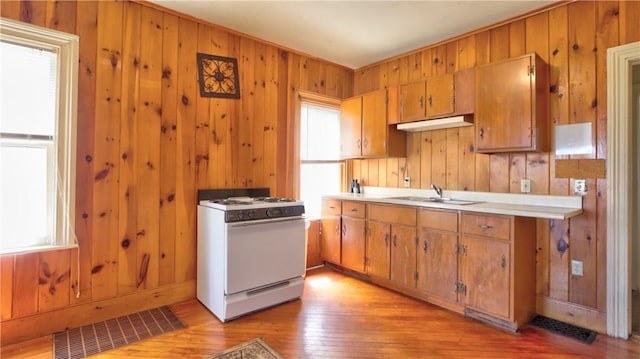 kitchen featuring brown cabinetry, a sink, wooden walls, and gas range gas stove