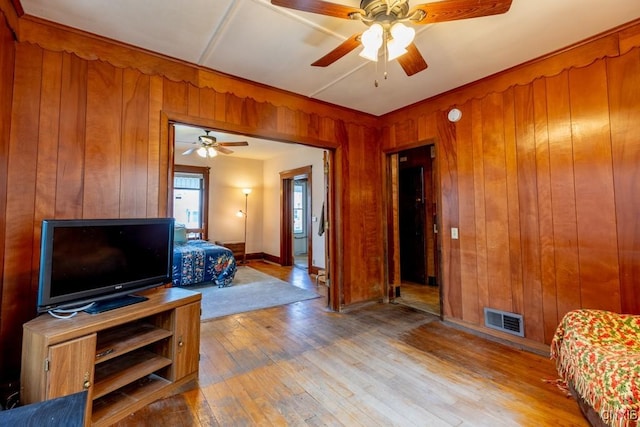 living area with hardwood / wood-style flooring, ceiling fan, wood walls, and visible vents