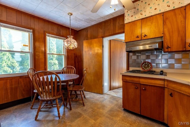 dining area featuring light floors, wooden walls, and ceiling fan with notable chandelier