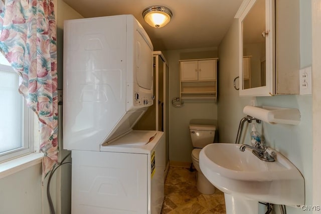 bathroom with stacked washer and dryer, baseboards, a sink, and toilet