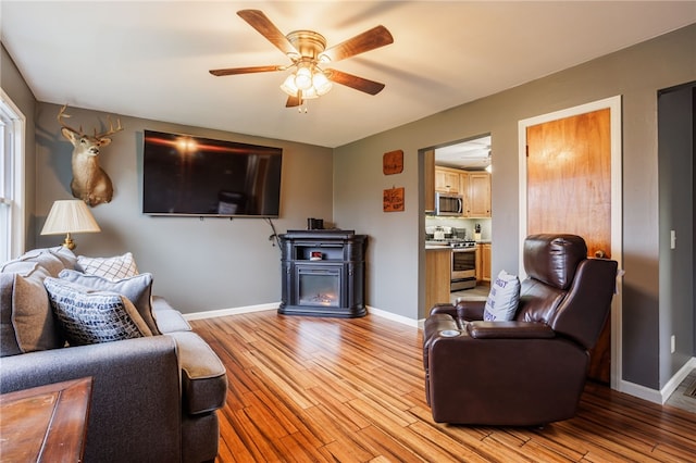 living room with light wood finished floors, baseboards, and ceiling fan