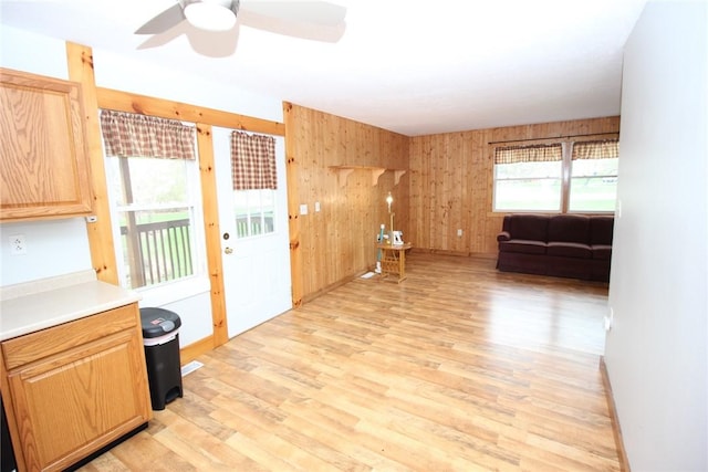 interior space featuring wooden walls, light wood finished floors, baseboards, and a ceiling fan