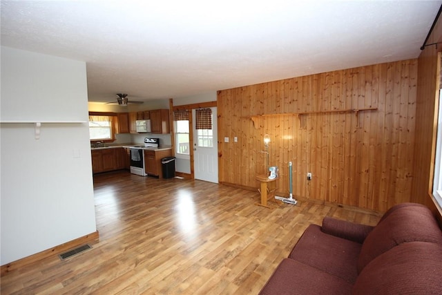 living room with light wood-type flooring, baseboards, visible vents, a ceiling fan, and wood walls