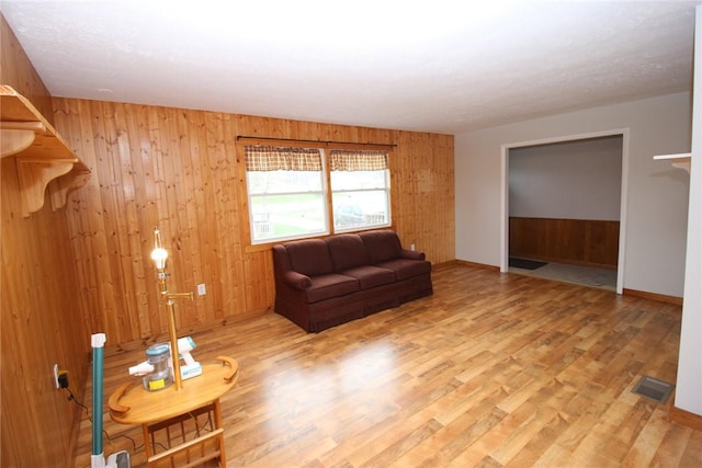 living room with wooden walls, baseboards, visible vents, and light wood-type flooring
