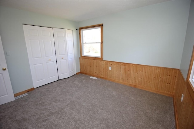 unfurnished bedroom featuring carpet flooring, wood walls, and wainscoting