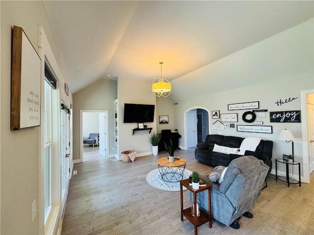 living room featuring arched walkways, vaulted ceiling, baseboards, and light wood-type flooring