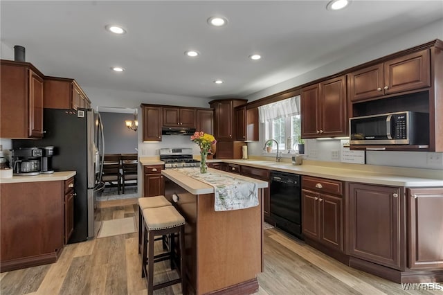 kitchen with a sink, appliances with stainless steel finishes, light countertops, under cabinet range hood, and a kitchen island