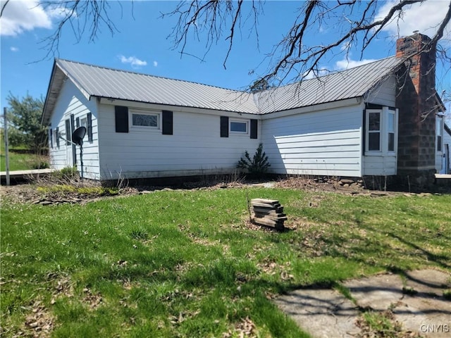 exterior space with a chimney, a yard, and metal roof