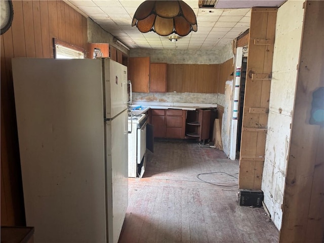 kitchen featuring brown cabinetry, hardwood / wood-style flooring, white appliances, and wooden walls