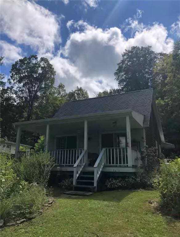 back of property with a lawn, covered porch, and roof with shingles