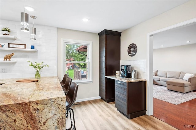 kitchen with backsplash, light stone counters, dark brown cabinets, and light wood-type flooring