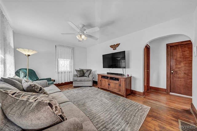 living room with arched walkways, ceiling fan, baseboards, and dark wood-style flooring