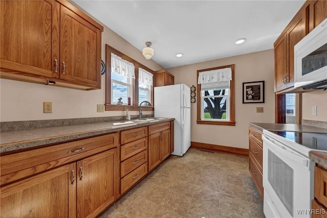 kitchen with brown cabinets, plenty of natural light, a sink, and white appliances