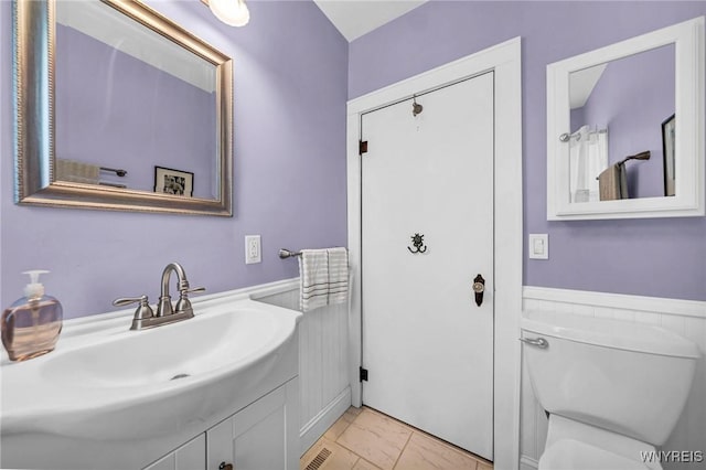 bathroom with toilet, vanity, and wainscoting