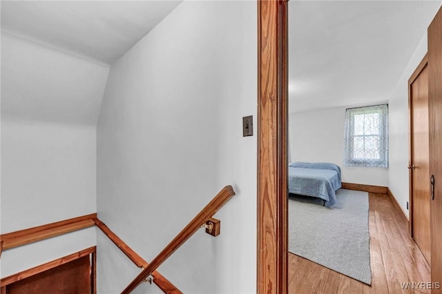corridor featuring light wood finished floors, an upstairs landing, and lofted ceiling