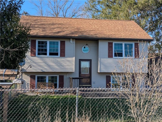 split foyer home featuring fence private yard, roof with shingles, and a front yard