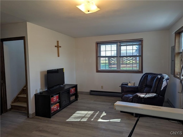sitting room featuring a baseboard heating unit, baseboards, wood finished floors, and electric panel