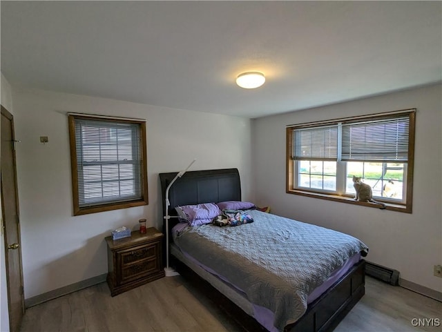 bedroom featuring a baseboard heating unit, baseboards, and light wood-style flooring