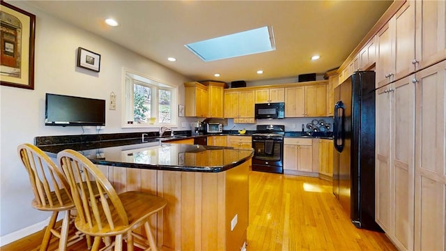 kitchen with light wood-type flooring, a skylight, black appliances, a peninsula, and a breakfast bar area