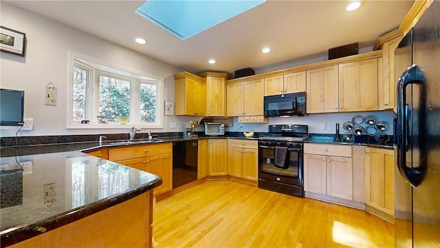 kitchen with light wood finished floors, a sink, dark stone counters, recessed lighting, and black appliances