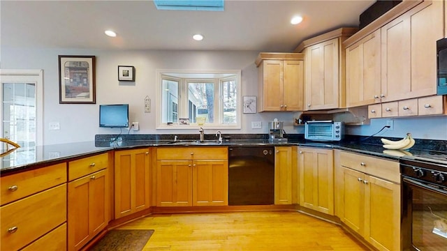 kitchen with a toaster, a sink, dark stone counters, black appliances, and light wood-style flooring